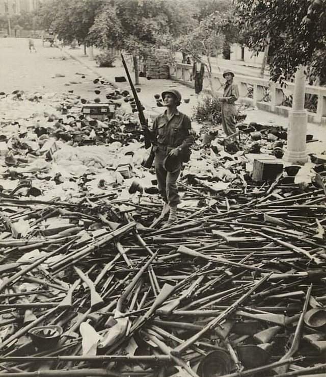 Солдат военной полиции США, стоящий на куче итальянских винтовок и шлемов после захвата Палермо, Сицилия, июль 1943 года.