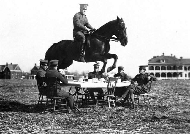 Американский офицер на лошади совершает прыжок через стол, за которым спокойно и небрежно сидят его сослуживцы.
