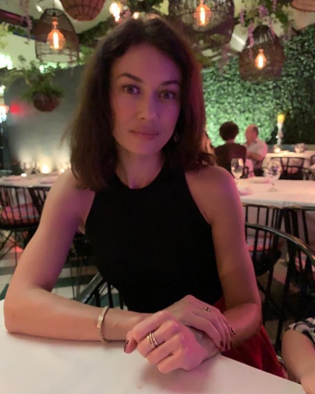 Ольга Куриленко в черной кофте и ювелирных украшениях на руках в ресторане
