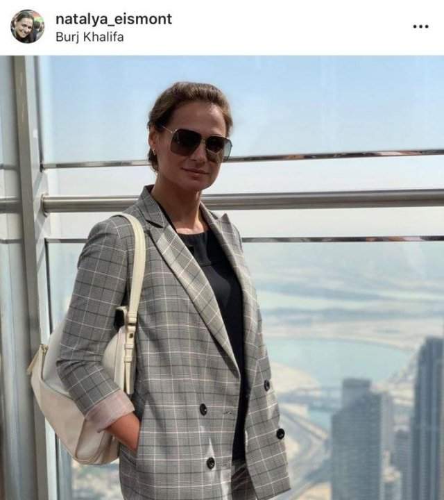 Наталья Эйсмонт в небоскребе в пиджаке в серую клетку и белой сумкой
