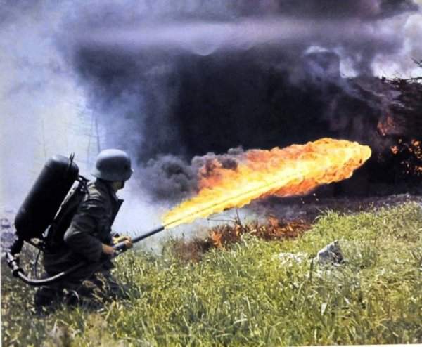 Немецкий солдат стреляет из ранцевого огнемета на поле высокой травы