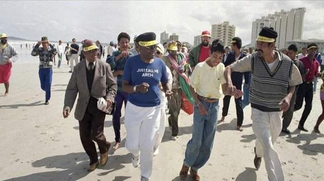 Вопреки законам апартеида, архиепископ Десмонд Туту (в голубом) и его сторонники бегают по белоснежному пляжу в Кейптауне. Южная Африка, 1989 год.
