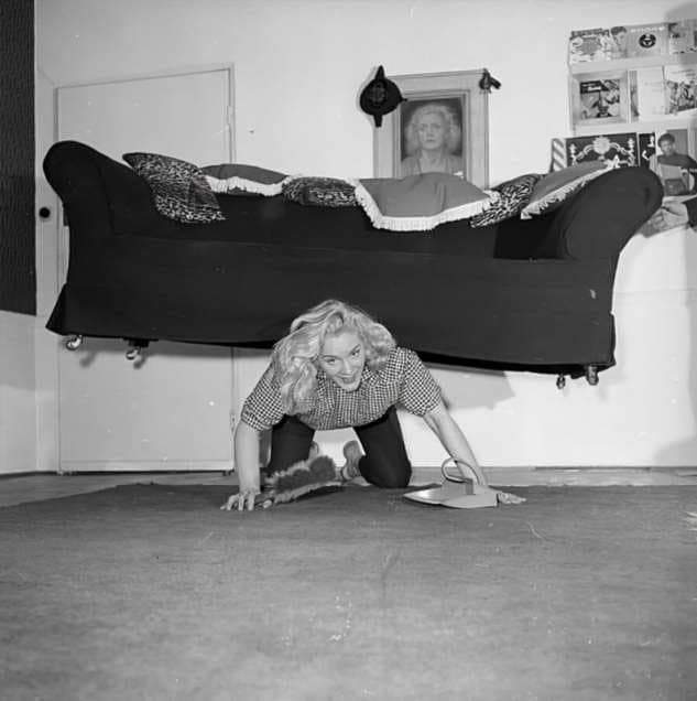 Английская цирковая силачка мисс Джоан Роудс поддерживает себя в форме занимаясь уборкой у себя в квартире, 1958 год.