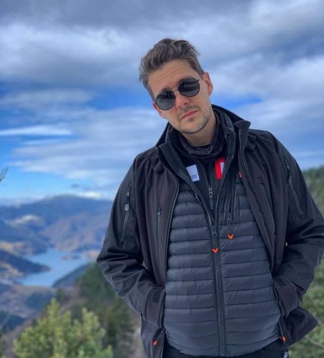 Милош Бикович в горах в куртке и очках