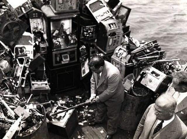 Мэр Нью-Йорка Фьорелло Ла Гуардиа разбивает кувалдой конфискованные игровые автоматы на борту полицейской лодки в Нью-йоркской гавани, 10 октября 1934 года.