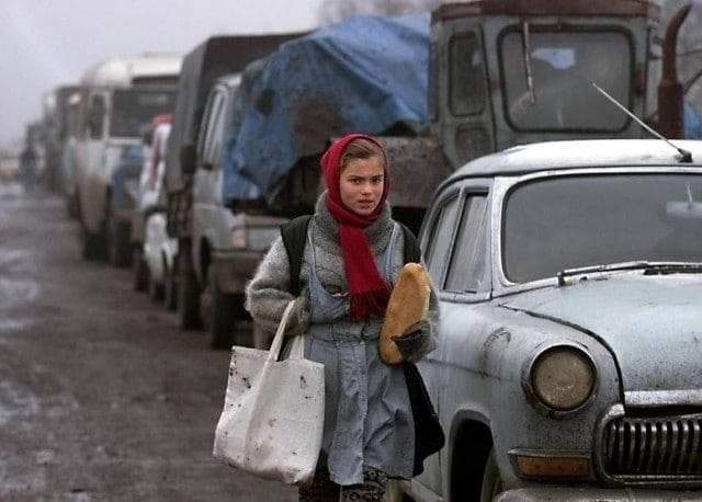 Девочка несёт буханку хлеба вдоль колонны беженцев, стоящих в очереди на контрольно-пропускном пункте у границы с Ингушетией, 27 декабря 1999 год.