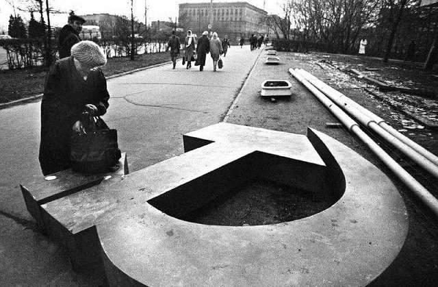 Женщина ищет что-то в сумке на поваленном серпе и молоте, Москве, 1991 год.